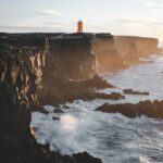 Oszałamiający widok na latarnię morską na nierównym wybrzeżu Islandii podczas zachodu słońca, ukazujący spektakularne klify i fale oceanu.