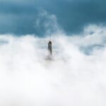 Islandia – informacje praktyczne przed wyjazdem Samotna latarnia morska stoi pośród morza chmur, tworząc spokojną i surrealistyczną scenę.