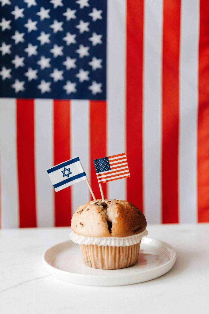 Muffin z flagami amerykańskimi i izraelskimi na tle flagi USA, symbolizujący stosunki międzynarodowe.