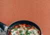 Świeża shakshuka na patelni z ziołami na stole. 