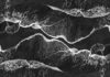 Oszałamiające monochromatyczne ujęcie lotnicze fal oceanicznych rozbijających się o brzeg, tworząc abstrakcyjne wzory.