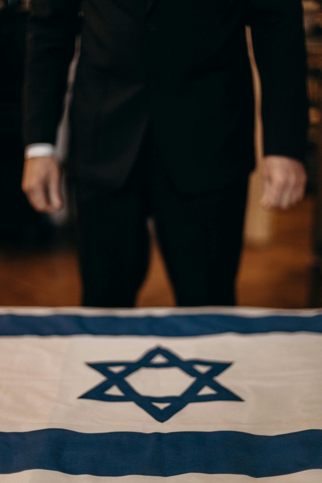 izrael Mężczyzna w garniturze stoi za stołem z powieszoną izraelską flagą.