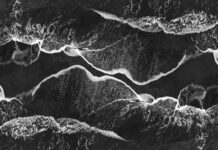Oszałamiające monochromatyczne ujęcie lotnicze fal oceanicznych rozbijających się o brzeg, tworząc abstrakcyjne wzory.