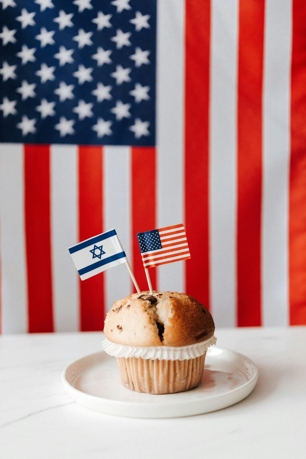 Muffin z flagami amerykańskimi i izraelskimi na tle flagi USA, symbolizujący stosunki międzynarodowe.