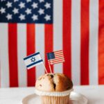 Loty do Izraela – które linie lotnicze wybrać? Muffin z flagami amerykańskimi i izraelskimi na tle flagi USA, symbolizujący stosunki międzynarodowe.