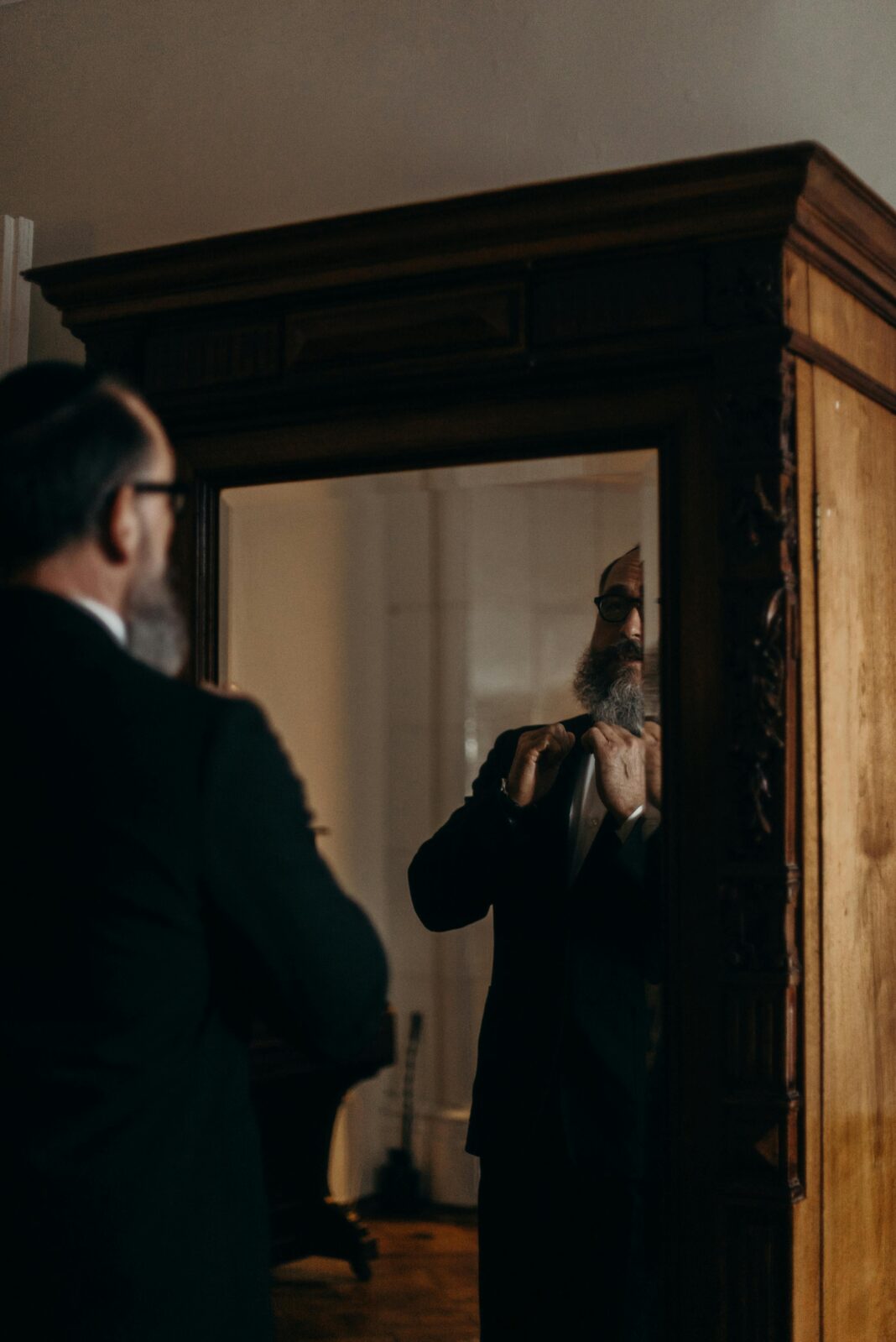 Mężczyzna poprawia krawat przed lustrem w stylu vintage, odzwierciedlając tradycję i elegancję.