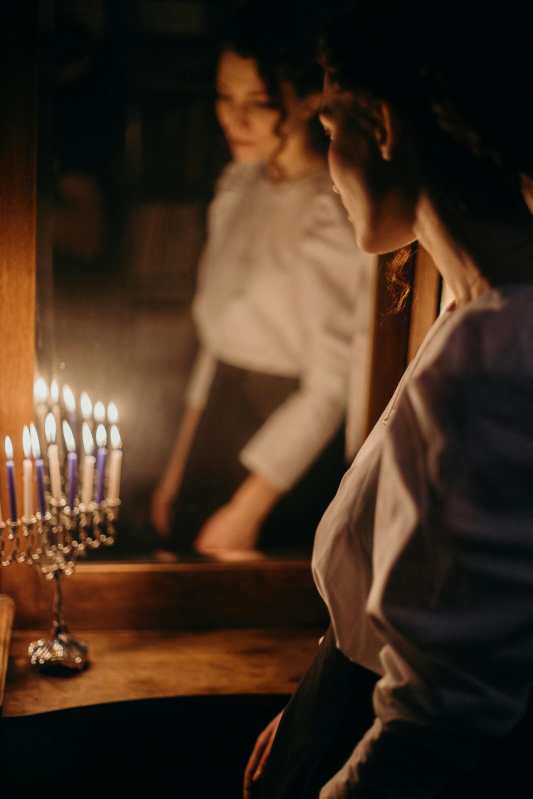 Kobieta odbijająca się w świetle świec, obserwująca menorę podczas święta żydowskiego.