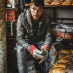 Młody mężczyzna pracujący w piekarni w Jerozolimie, otoczony świeżo upieczonym chlebem.