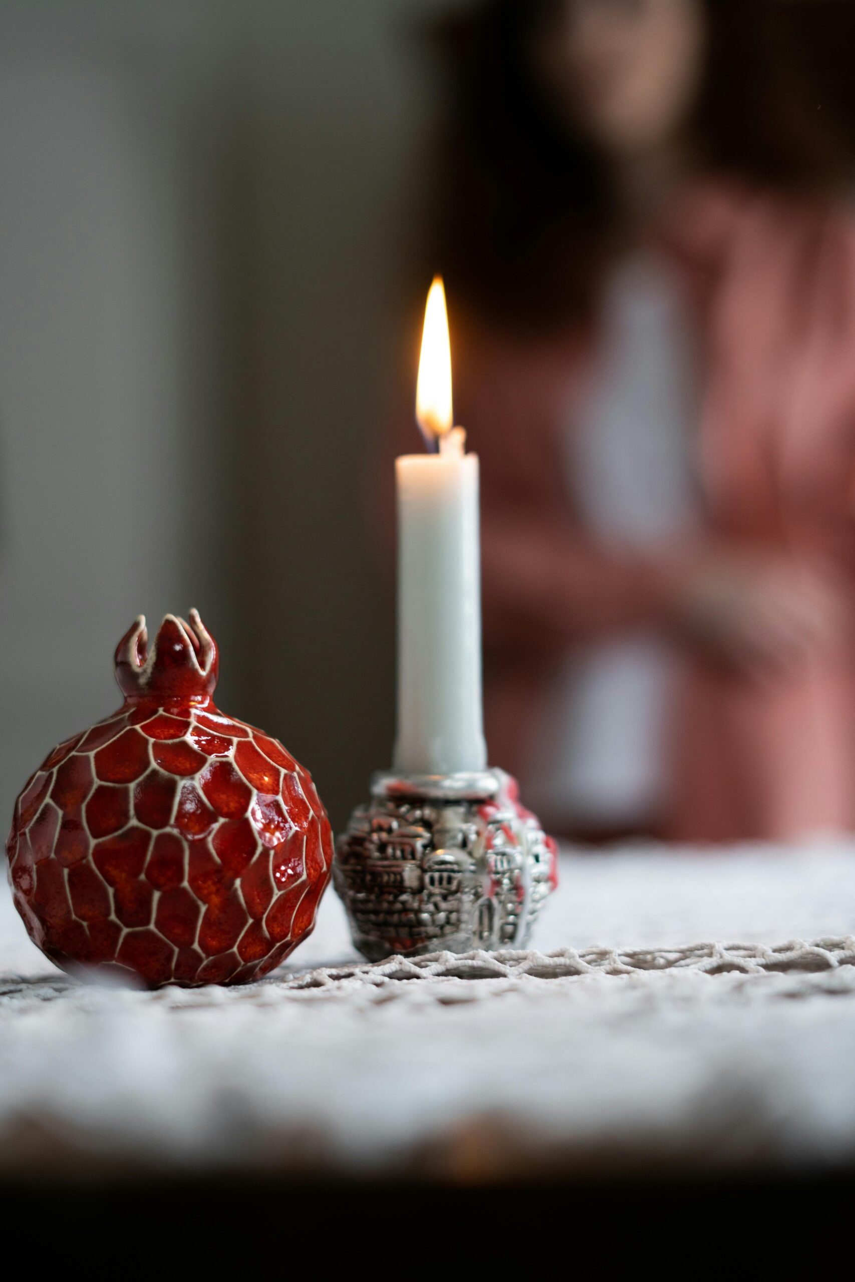 Elegancka martwa natura z ceramicznym granatem i świecą na koronkowym obrusie.