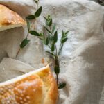 Widok z góry pokrojonego chałki z liśćmi na lnianym obrusie, oznaczający tradycję.