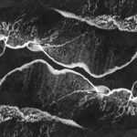 Oszałamiające monochromatyczne ujęcie lotnicze fal oceanicznych rozbijających się o brzeg, tworząc abstrakcyjne wzory.