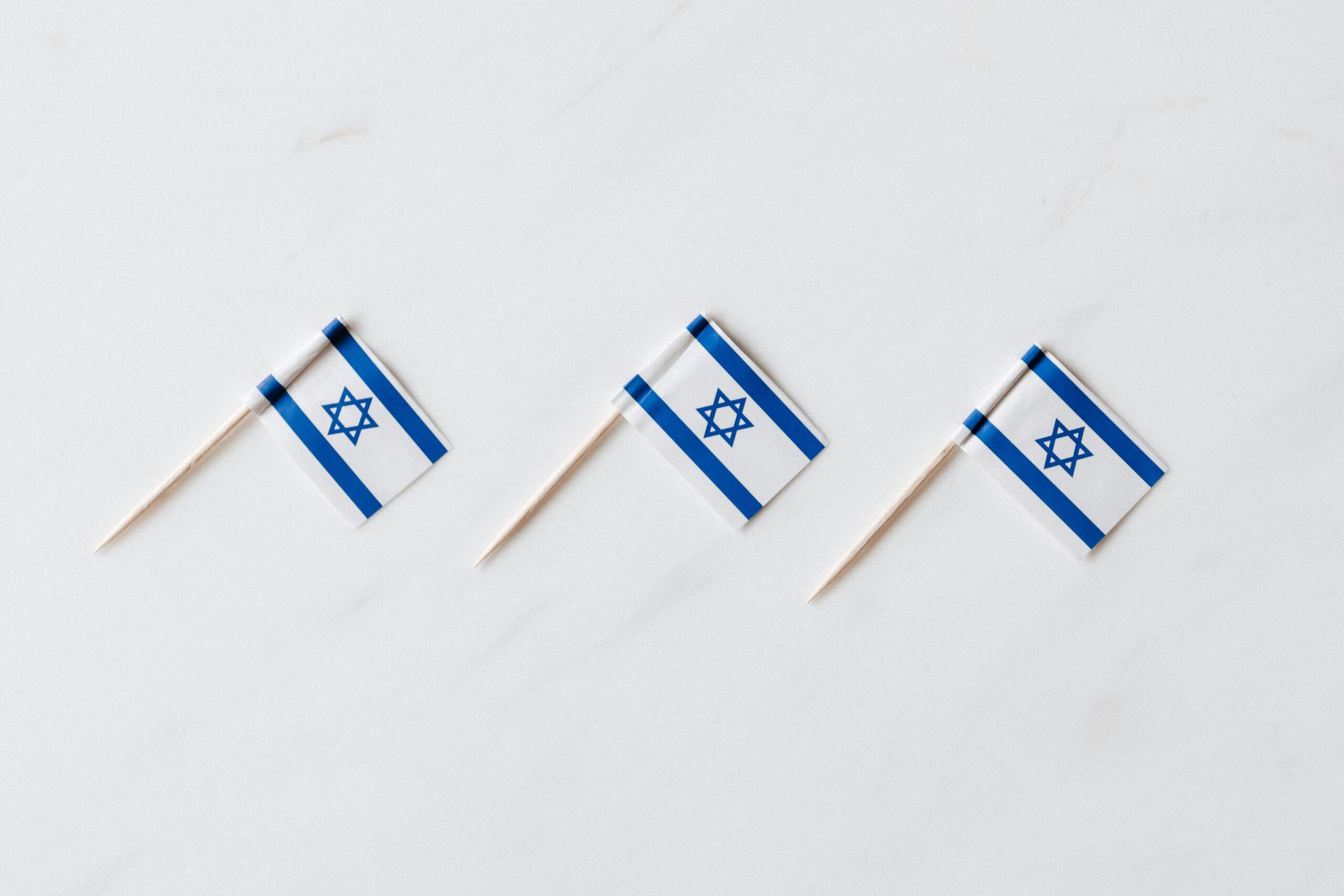 Minimalistyczna ekspozycja trzech wykałaczek z flagą Izraela na białym tle symbolizujących dumę narodową.