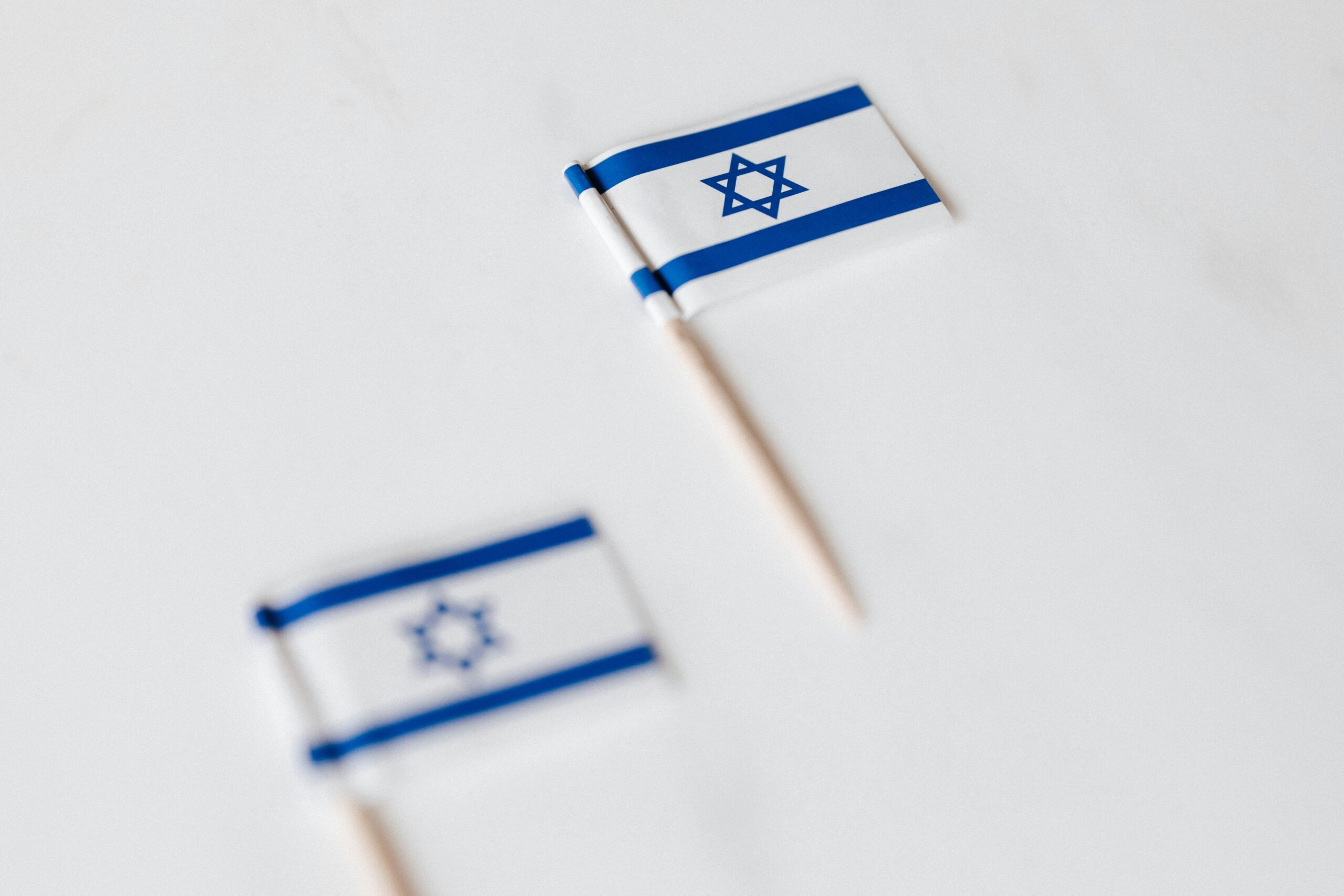 Zbliżenie dwóch miniaturowych izraelskich flag na wykałaczkach z białym tłem.