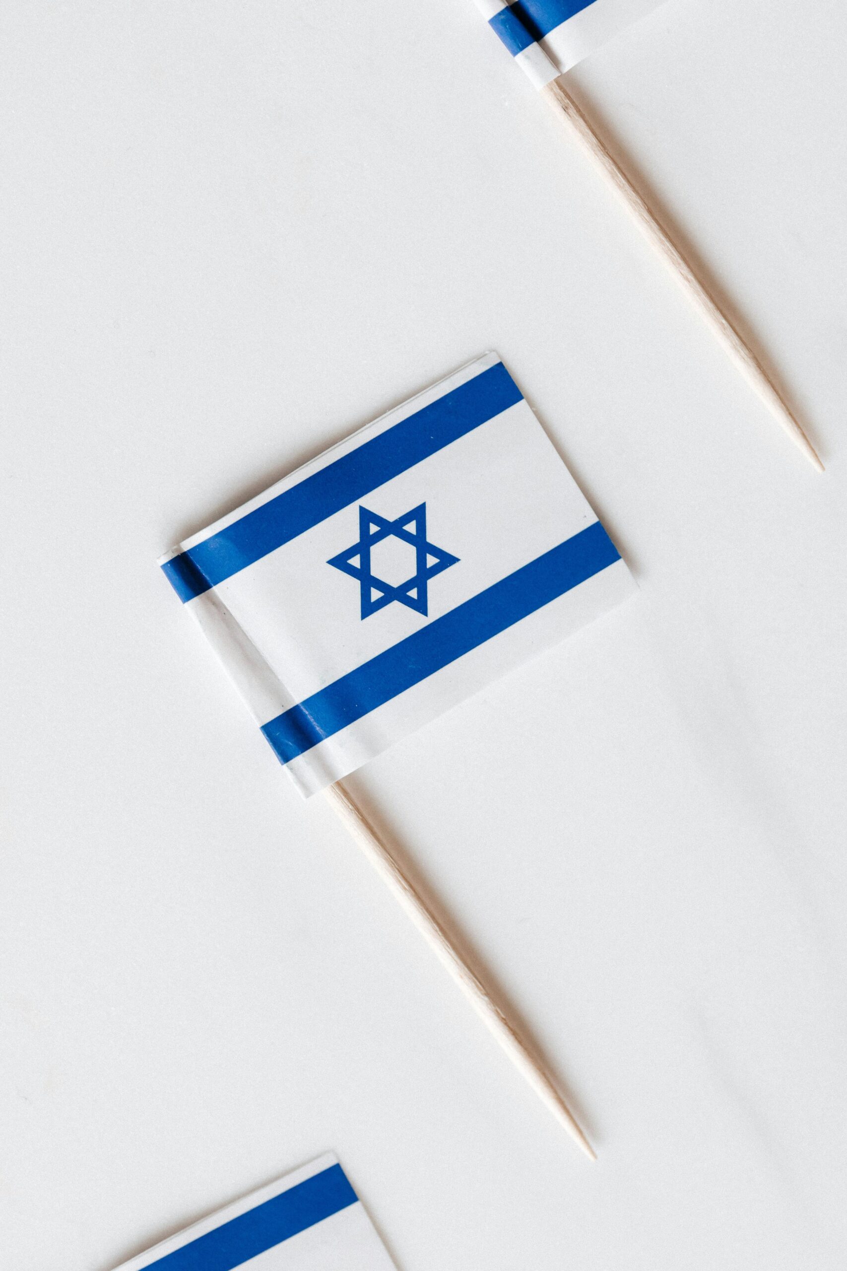 Widok z góry zbiór małych papierowych flag Izraela na wykałaczkach umieszczonych w linii na białej powierzchni
