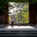 Tateyama Kurobe Alpine Route: Śnieżne korytarze i spektakularne widoki Rodzina spaceruje przez bramę świątyni otoczoną bujną zielenią w Kioto w Japonii.