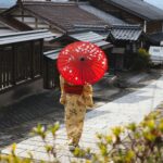 Arashiyama Bamboo Grove: Spacer wśród magicznego lasu bambusowego Kobieta w kimonie z czerwonym parasolem spacerująca tradycyjną japońską ulicą w wiosce.