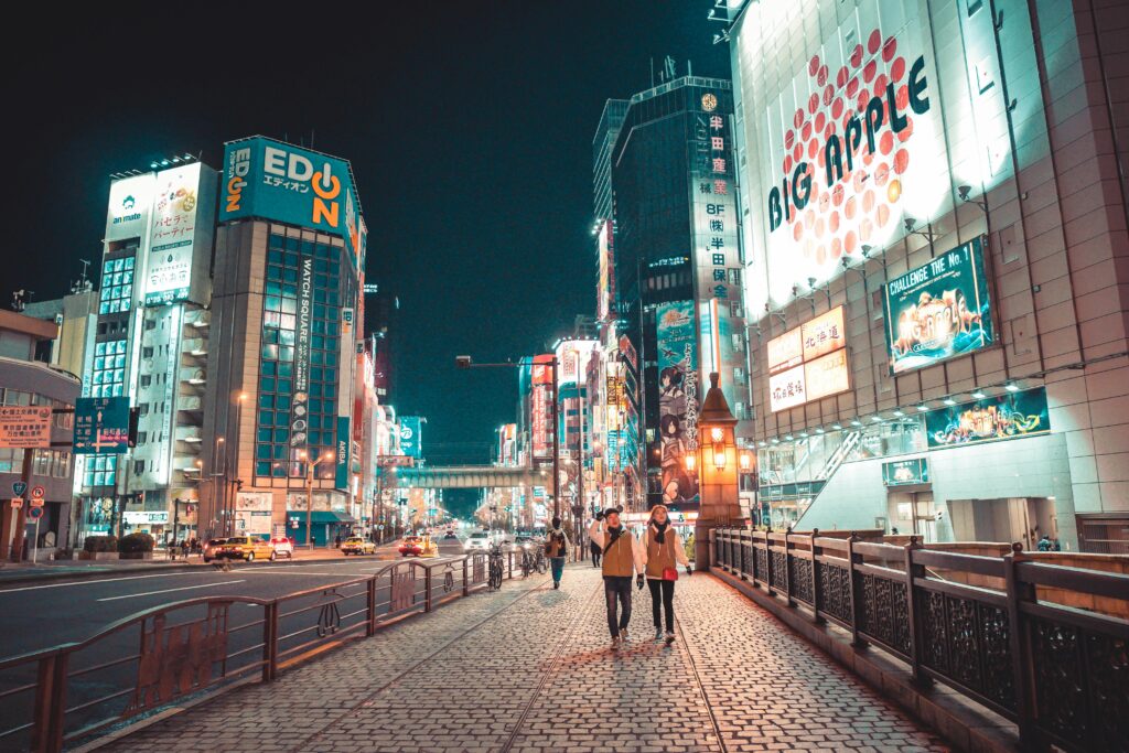 Miejski pejzaż miejski Japonii nocą z oświetlonymi budynkami i ludźmi spacerującymi ulicą.