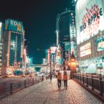 Otaru: Kanały, weneckie szkło i świeże owoce morza Miejski pejzaż miejski Japonii nocą z oświetlonymi budynkami i ludźmi spacerującymi ulicą.