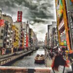 Jesień w Japonii: Najlepsze miejsca na podziwianie czerwonych liści Tętniąca życiem scena w Dotonbori, ukazująca łodzie i kupujących pod dramatycznym niebem w Osace.