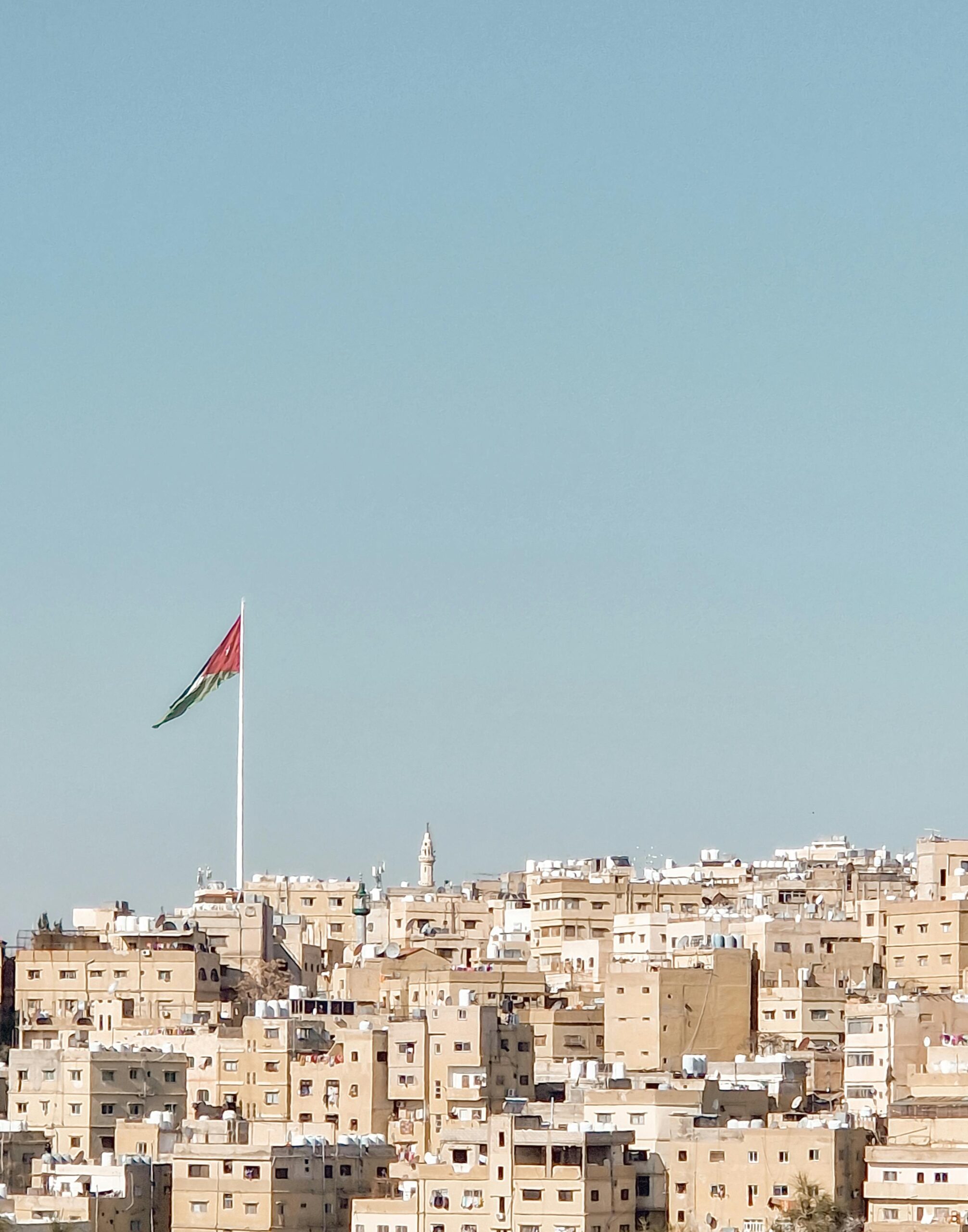 Widok na pejzaż Ammanu z budynkami i flagą Jordanii pod czystym niebem.