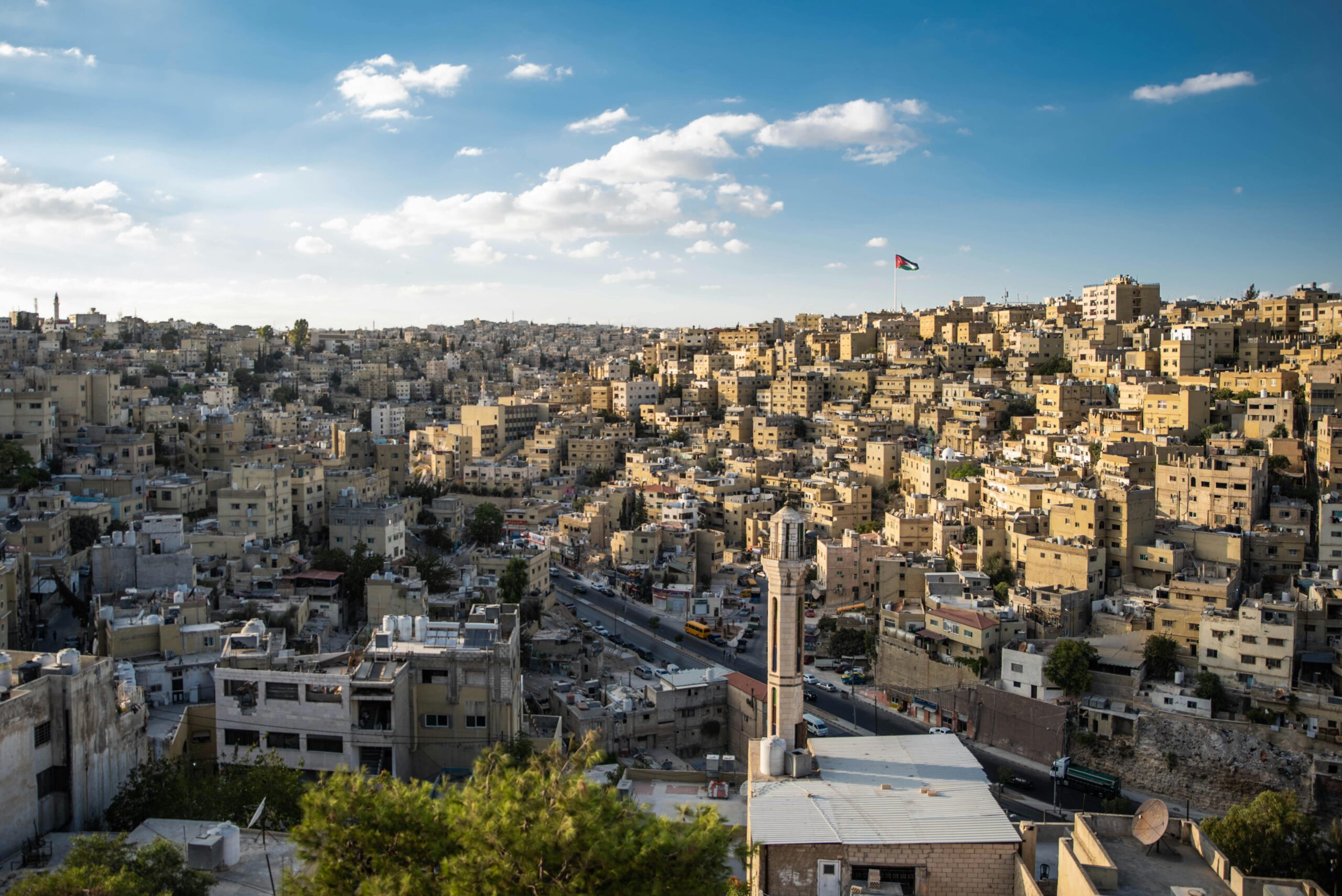 Widok z lotu ptaka na miejski krajobraz Ammanu z powiewającą flagą Jordanii.