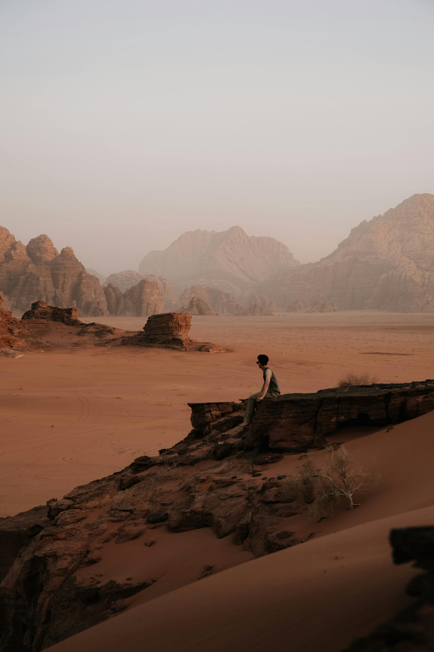 Mężczyzna siedzi na skale w majestatycznym pustynnym krajobrazie Wadi Rum o zachodzie słońca.