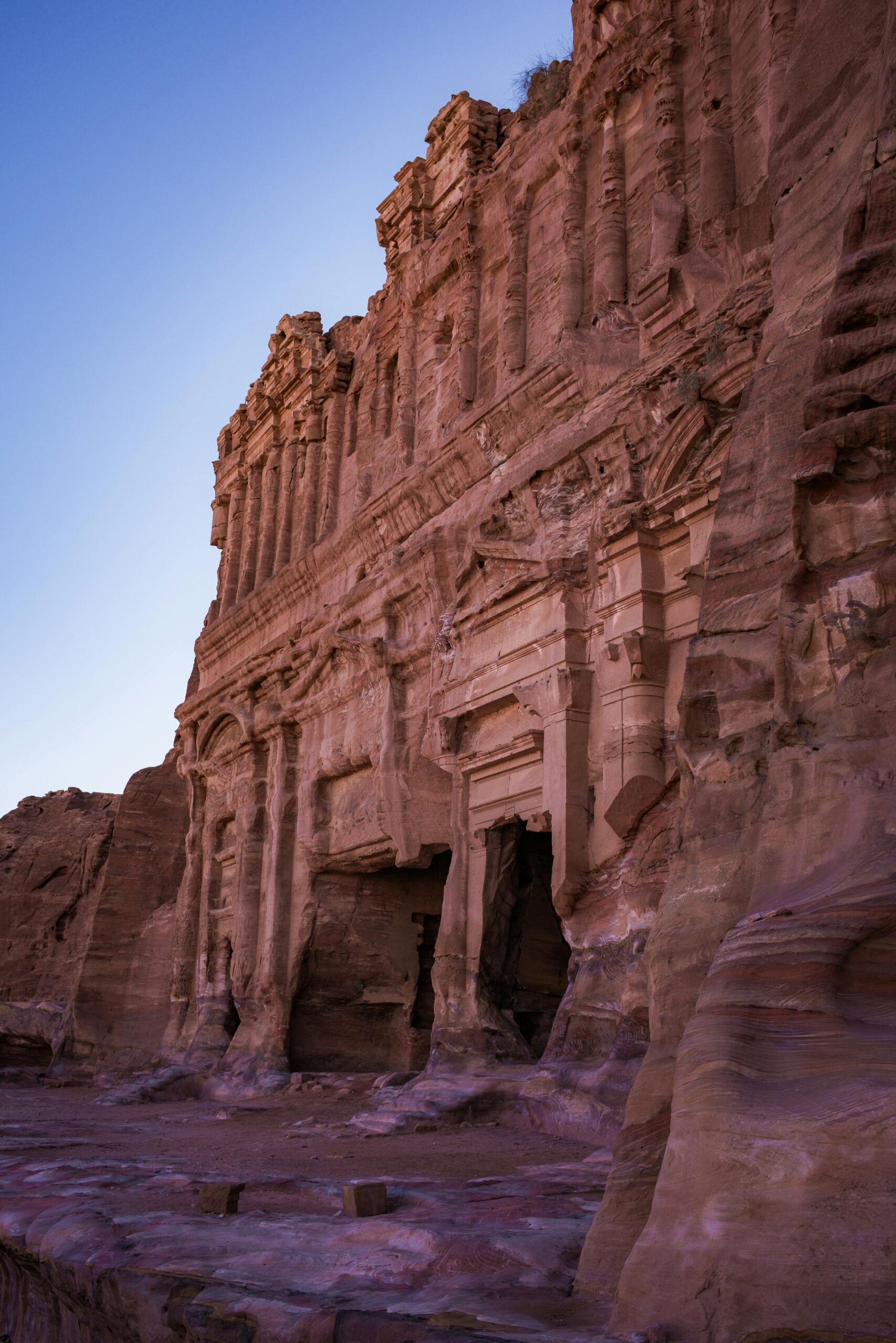 Ujęcie majestatycznej fasady grobowca pałacowego w Petrze, odsłaniającej misterne rzeźby z piaskowca pod czystym niebem o zachodzie słońca.