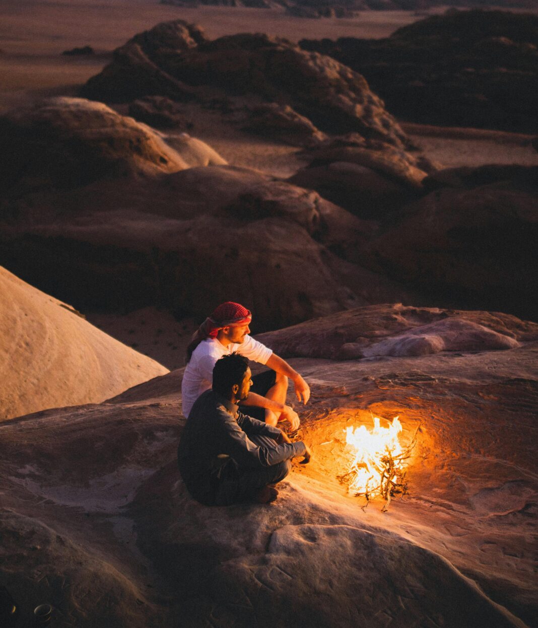 Dwóch mężczyzn siedzących przy ognisku na tle pięknej pustyni Wadi Rum o zachodzie słońca.