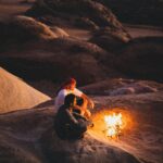 Dwóch mężczyzn siedzących przy ognisku na tle pięknej pustyni Wadi Rum o zachodzie słońca.