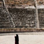 Kobieta w abai stojąca w starożytnym rzymskim teatrze w Jordanii, oferująca perspektywę historyczną.