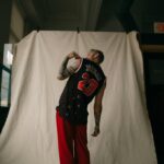 Widok z tyłu mężczyzny w koszulce Jordan z tatuażami, stojącego w pomieszczeniu.