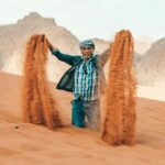 Święta religijne w Jordanii – Ramadan i Eid Poważny etniczny brodaty starzec wylewający piasek z rąk klęczących na gorącej pustyni