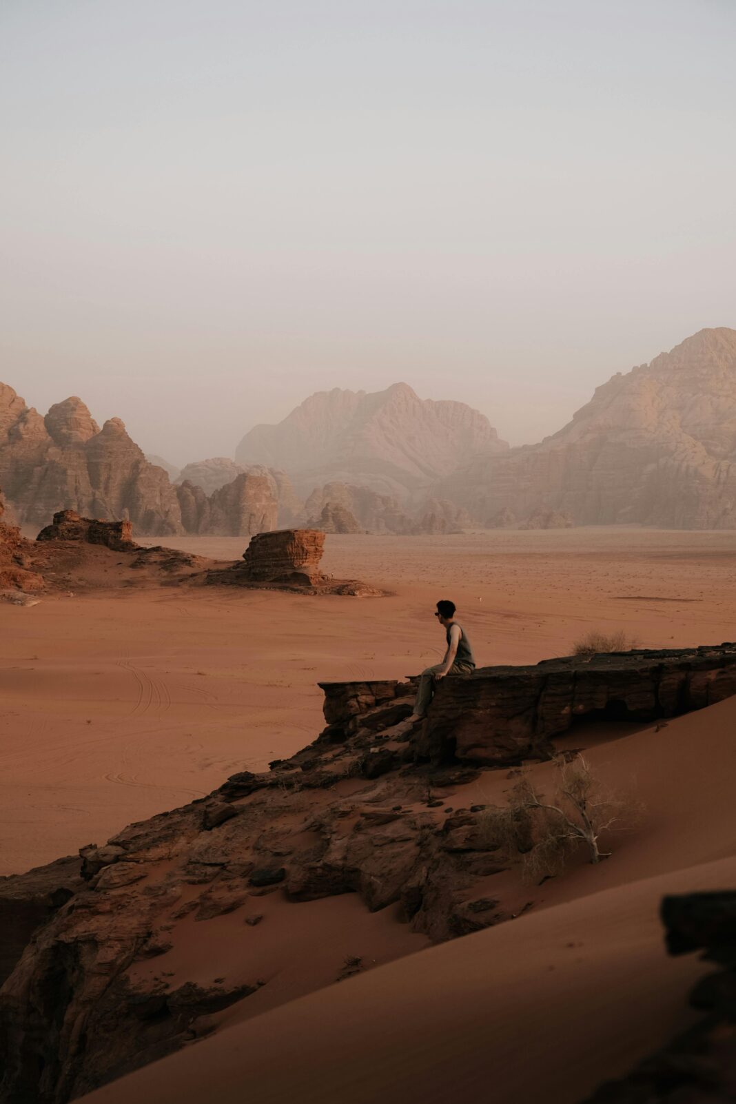 Mężczyzna siedzi na skale w majestatycznym pustynnym krajobrazie Wadi Rum o zachodzie słońca.