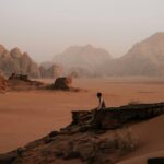 Mężczyzna siedzi na skale w majestatycznym pustynnym krajobrazie Wadi Rum o zachodzie słońca.