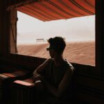 Jordania dla backpackerów – poradnik taniego podróżowania Mężczyzna wygląda przez pustynne okno z wydmami w tle, tworząc nastrojową sylwetkę.