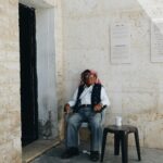 Starszy mężczyzna ubrany w tradycyjny strój, siedzący przy kamiennym murze w Ammanie, oferujący wgląd w kulturę jordańską.