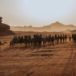 Urzekający widok karawany wielbłądów przemierzającej pustynię Wadi Rum o zachodzie słońca.