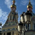 Ozdobne wieże kościelne ze złotymi kopułami i latarniami ulicznymi pod błękitnym niebem.