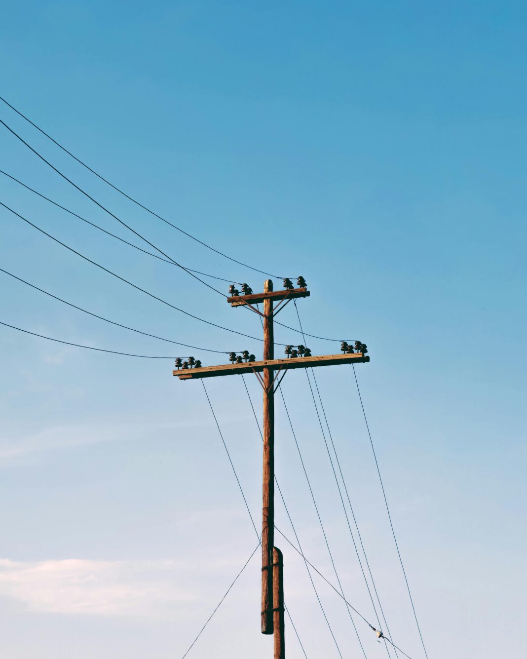 Słup elektryczny z liniami energetycznymi pod czystym, błękitnym niebem, minimalne chmury.