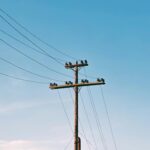 Słup elektryczny z liniami energetycznymi pod czystym, błękitnym niebem, minimalne chmury.