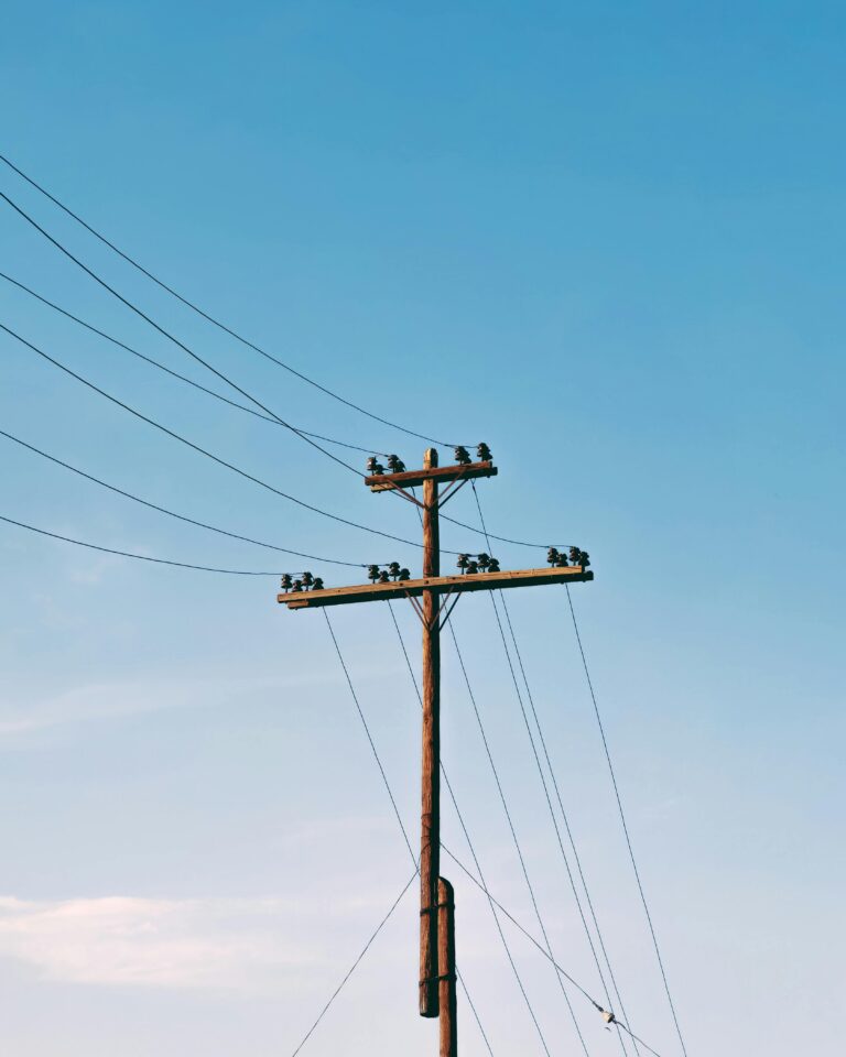 Słup elektryczny z liniami energetycznymi pod czystym, błękitnym niebem, minimalne chmury.