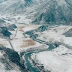 Tamgaly-Tas: Mistyczne petroglify nad rzeką Ili Oszałamiające zdjęcie lotnicze przedstawiające wijącą się rzekę pośród pokrytych śniegiem gór i dolin.