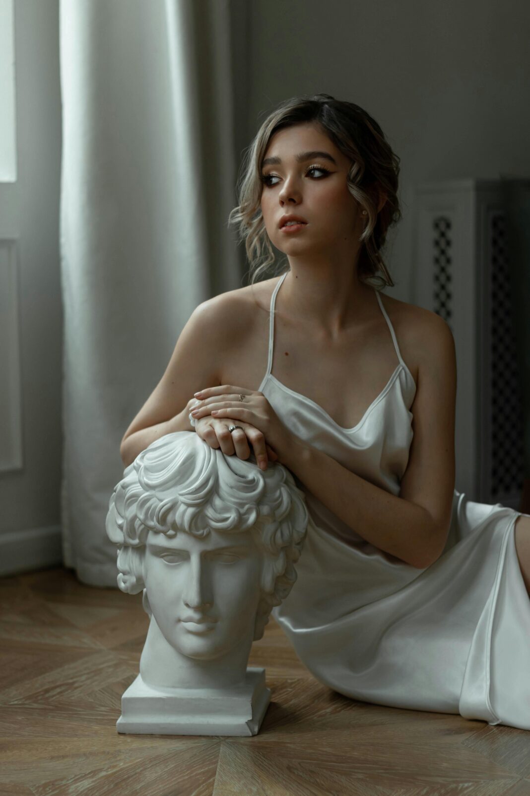 Stylowa kobieta w jedwabnej sukience pozuje z biustem w pomieszczeniu. 