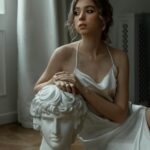 Stylowa kobieta w jedwabnej sukience pozuje z biustem w pomieszczeniu. 