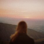 Bajkonur: Kolebka eksploracji kosmosu Sylwetka kobiety z widokiem na góry Ałmaty o zachodzie słońca, tworząc spokojny krajobraz.