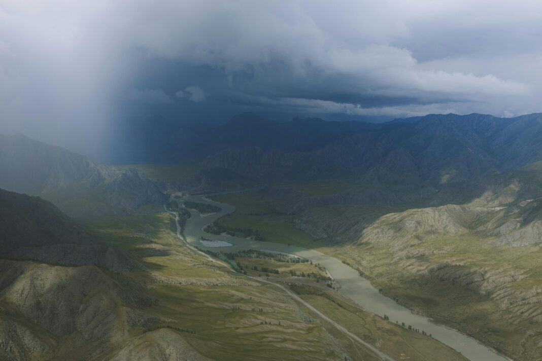 Widok z lotu ptaka na rzekę wijącą się przez dramatyczny górski krajobraz pod burzliwymi chmurami.