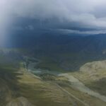 Widok z lotu ptaka na rzekę wijącą się przez dramatyczny górski krajobraz pod burzliwymi chmurami.