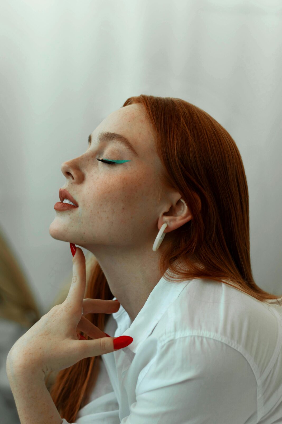 Piękna rudowłosa kobieta z niebieskim eyelinerem pozuje w studiu profilowym.