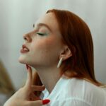 Piękna rudowłosa kobieta z niebieskim eyelinerem pozuje w studiu profilowym.