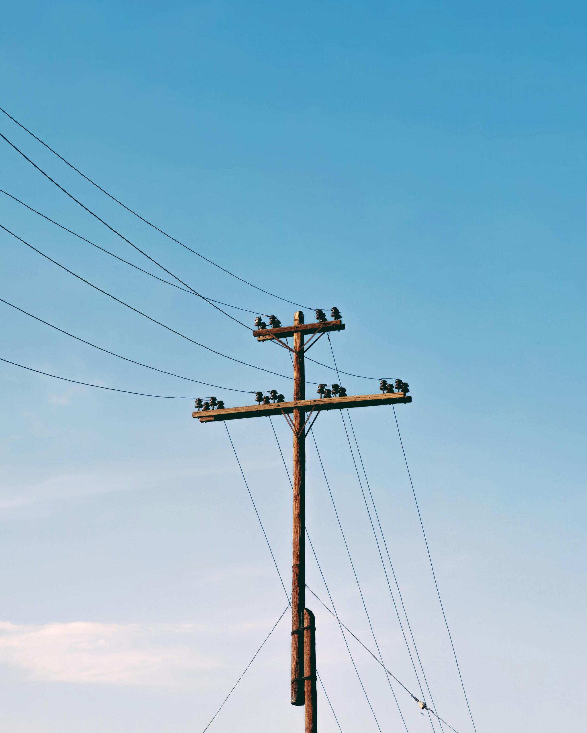 Słup elektryczny z liniami energetycznymi pod czystym, błękitnym niebem, minimalne chmury.